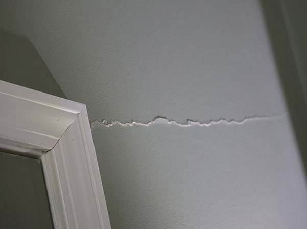 Stairstep crack in wall near door frame, indicating foundation movement and potential structural stress.