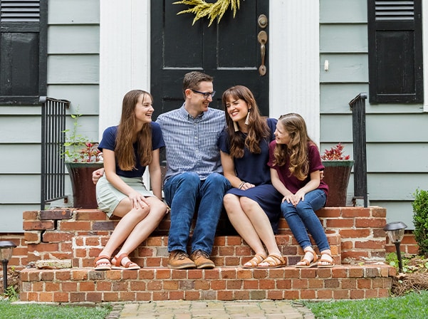 Family smiling on front porch steps, stable home foundation and long-term security.